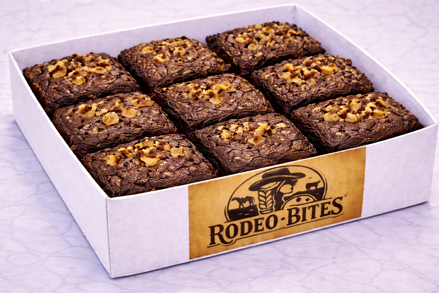 Box of Rodeo Bites brownies with pecans in a Rodeo Bites box on a marble surface.