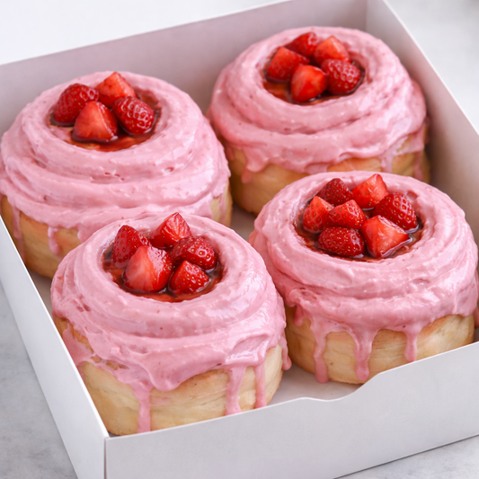 Four pink frosted pastries with strawberry toppings in a white box.